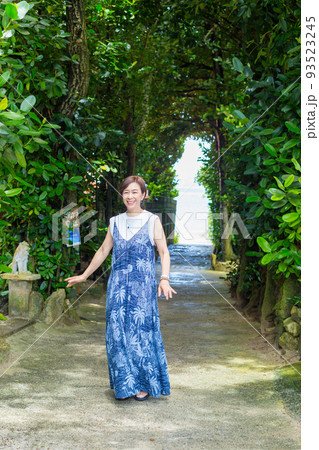 樹齢数百年のフクギの木が並ぶ砂の道を歩く旅ガール、沖縄のパワースポット「フクギ並木」 93523245