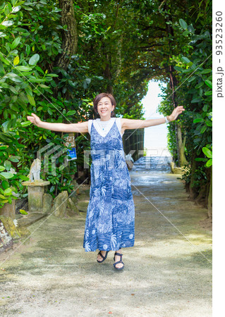 樹齢数百年のフクギの木が並ぶ砂の道を歩く旅ガール、沖縄のパワースポット「フクギ並木」 93523260