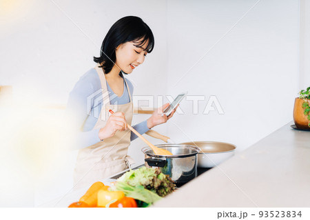 スマホを見ながら料理する女性 93523834