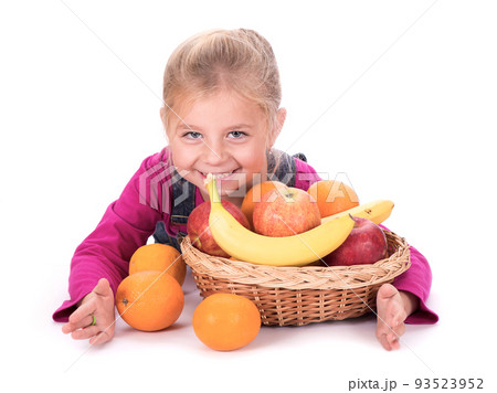 Close-up portrait of a little girl holding fruits - apples, bananas and oranges. Isolated on a light background. 93523952