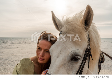 A young woman and a white horse against the background of the sky and the sea. 93524276