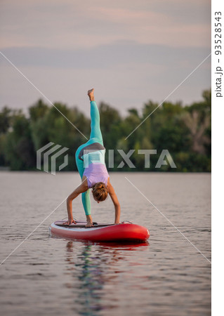 Sporty woman in yoga position on paddleboard, doing yoga on sup board, exercise for flexibility and stretching of muscles 93528543