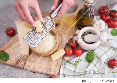 Woman grates Parmesan cheese on a wooden cutting board at domestic kitchen 93530504