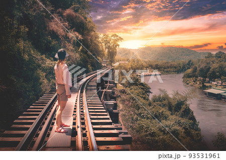 Woman standing on The Historical Death Railway Of World War 2 in River Kwai Kanachanaburi, country side of Thailand. with dramatic sunset. Woman standing on The Historical Death Railway Of World War 2 in River Kwai Kanachanaburi, country side of Thailand. with dramatic sunset. 93531961