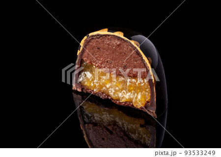 Cut luxury handmade candy with chocolate and yellow confiture filling on black background. Cut luxury handmade candy with chocolate and yellow confiture filling on black background. 93533249