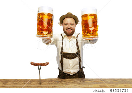 Portrait of smiling man wearing traditional Bavarian or German clothes and giving big mugs with foamy beer isolated over white background Portrait of smiling man wearing traditional Bavarian or German clothes and giving big mugs with foamy beer isolated over white background 93535735