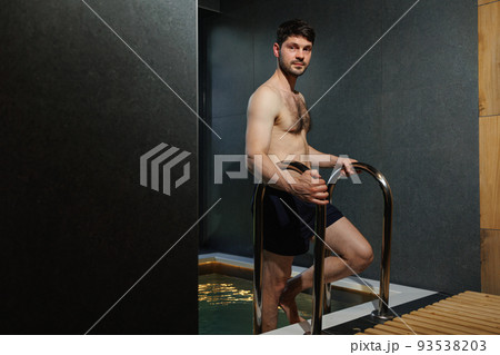 Muscular man descends into the pool in the spa complex Muscular man descends into the pool in the spa complex 93538203
