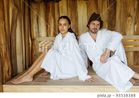 Portrait of young man and woman sitting on wooden bench in sauna Portrait of young man and woman sitting on wooden bench in sauna 93538388