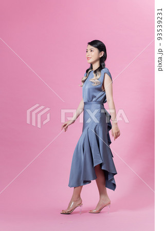 Full length portrait of a pretty young woman wearing blue dress and high heels isolated on a pink background 93539231