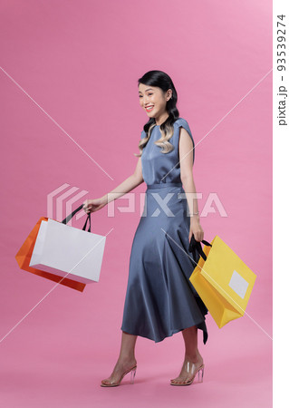 young beautiful woman in blue dress, holding colourful shopping bags, isolated over pink background 93539274