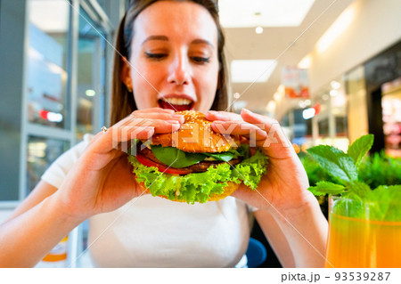 Vegetarian hamburger healthy vegan burger. Cute cheerful girl eating veggie sandwich with salad, avocado, vegetable. Vegan burger healthy diet food. 93539287