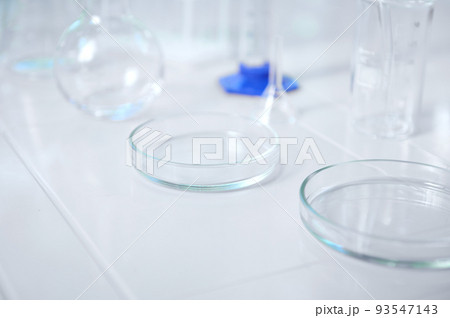 Focus on a glass lab plate - a Petri dish on a white table on the blurred background labware for biochemical experiment. Chemistry set in a scientific biological and chemical laboratory. Copy ad space 93547143