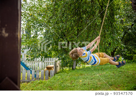 Happy little boy is having fun on a rope swing which he has found while having rest outside city. Active leisure time with children Happy little boy is having fun on a rope swing which he has found while having rest outside city. Active leisure time with children 93547570