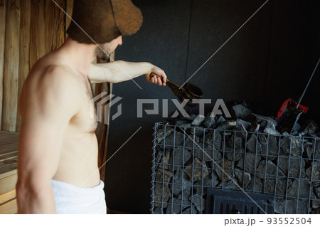 Man pouring water into hot stone in sauna room Man pouring water into hot stone in sauna room 93552504