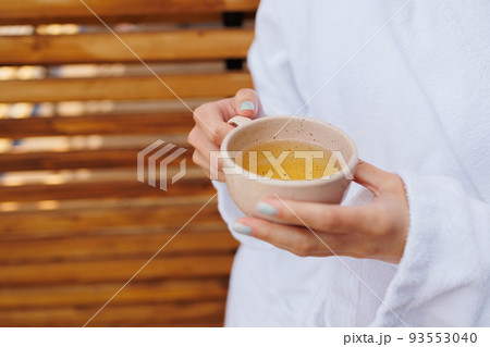 Woman in bathrobe holding a cup of tea in her hands Woman in bathrobe holding a cup of tea in her hands 93553040