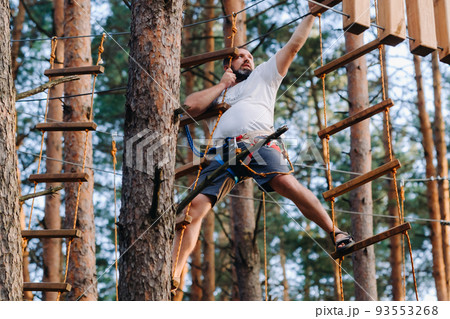 A man overcomes an obstacle in a rope town. A man in a forest rope park A man overcomes an obstacle in a rope town. A man in a forest rope park 93553268