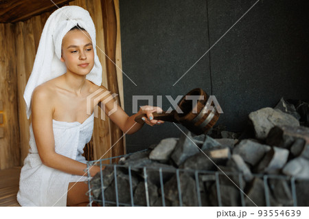 Young woman is pouring water into hot stone in sauna 93554639