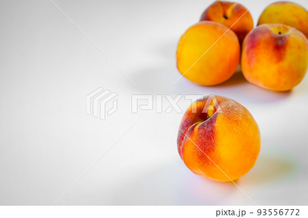 One ripe beautiful peach close-up in the foreground on the right and several peaches behind it in a blur in the right corner on a white background, space for text on the left One ripe beautiful peach close-up in the foreground on the right and several peaches behind it in a blur in the right corner on a white background, space for text on the left 93556772