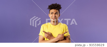 Close-up portrait of insecure, indecisive young hispanic man cant make up his mind, deciding between two variants, dont know what choose, need help with decision, pointing fingers left and right 93559029