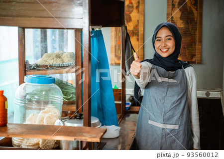 excited hijab woman wearing apron standing with thumbs up 93560012