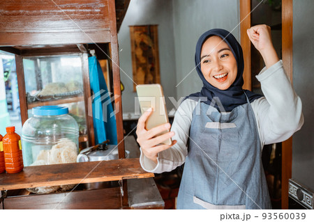 veiled woman wearing an apron happily looking at her cellphone veiled woman wearing an apron happily looking at her cellphone 93560039