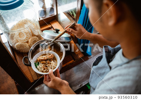 man seller put chicken topping over noodles in a bowl 93560310