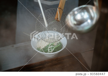 hands of seller pouring into the bowl of boiled noodles 93560447