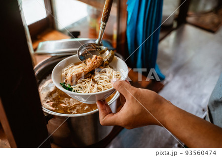 close up of seller's hand put chicken on noodles 93560474