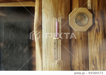 Sand timer and thermometer with hygrometer hanging on the wooden wall of the sauna 93584572