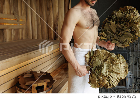 Man with leaf broom in sauna 93584575