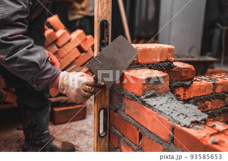 Bricklayer puts bricks to make a wall. 93585653