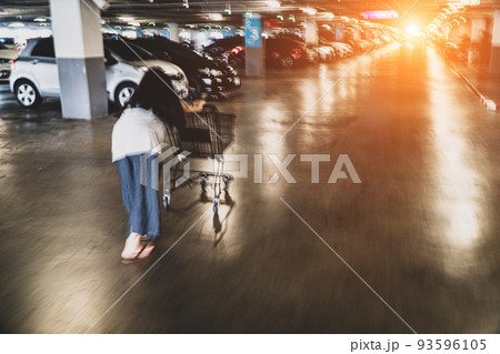 Blur the image of the back of a teenage girl pushing a shopping cart quickly in a supermarket-shaded parking building, moving forward at speed. Young women push cart empty shopping. 93596105