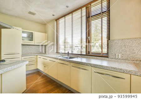 Interior of light kitchen with modern cupboards and appliances located near dining room in modern flat at daytime Interior of light kitchen with modern cupboards and appliances located near dining room in modern flat at daytime 93599945