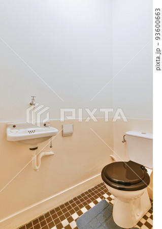 Interior of narrow restroom with sink and wall hung toilet with white walls and checkered floor Interior of narrow restroom with sink and wall hung toilet with white walls and checkered floor 93600663