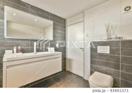 Modern flush toilet and ceramic sink installed on white tiled walls near mirror and towel in small restroom at home Modern flush toilet and ceramic sink installed on white tiled walls near mirror and towel in small restroom at home 93601371