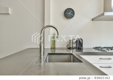 Sink with shiny tap installed under modern counter near jar with spices and gas stove in kitchen at home Sink with shiny tap installed under modern counter near jar with spices and gas stove in kitchen at home 93602162