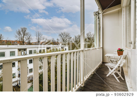 Narrow brick balcony with metal railings, wooden chair and door 93602929