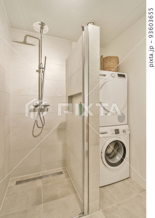 Shower faucets attached to tiled wall near glass partition and washing machine in washroom at home Shower faucets attached to tiled wall near glass partition and washing machine in washroom at home 93603655