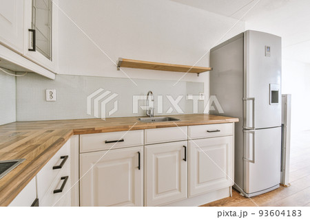Fragment of interior of light narrow home kitchen with minimalist style white furniture with sink and stove Fragment of interior of light narrow home kitchen with minimalist style white furniture with sink and stove 93604183