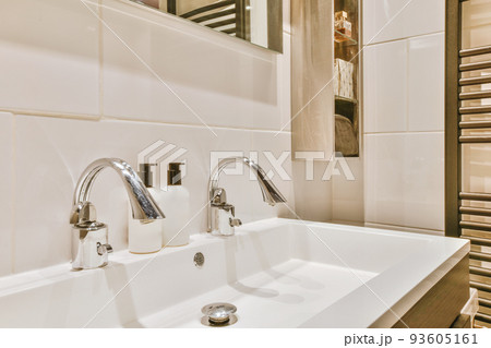 Sink with tap and liquid soap hanging on tiled wall under mirror in contemporary restroom at home 93605161