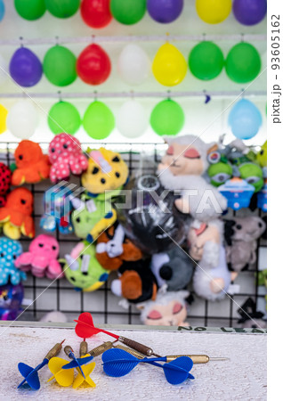 selective focus on darts sitting on a ledge with a wall of balloon targets and prizes that a player can win at a fair. 93605162