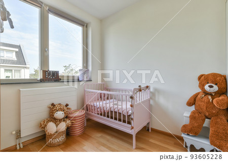 Interior of white room with baby crib and armchair near window with blue chest of drawers in daylight Interior of white room with baby crib and armchair near window with blue chest of drawers in daylight 93605228