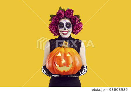 Joyful woman with creative traditional Mexican make-up holding glowing Halloween pumpkin. Joyful woman with creative traditional Mexican make-up holding glowing Halloween pumpkin. 93608986