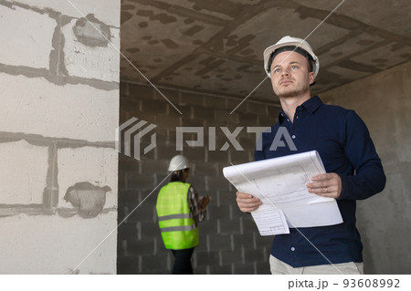 male chief engineer and a female assistant are taking measurements indoors. two engineers, a man and a woman in white helmets and protective vests, male chief engineer and a female assistant are taking measurements indoors. two engineers, a man and a woman in white helmets and protective vests, 93608992