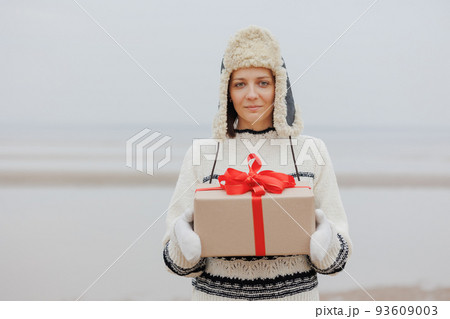 woman in a Santa Claus hat with a gift box in her hands smiles. a happy European woman carries a gift for New Year or Christmas. 93609003