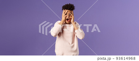 Portrait of shocked, startled handsome man being embarrassed and scared of seeing something unappropriate and awkward, cover eyes but peeking through fingers from interest 93614968