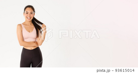 Sport, wellbeing and active lifestyle concept. Smiling pretty asian girl in sportswear, playing with ponytail and looking happy at camera after good gym workout, standing white background 93615014