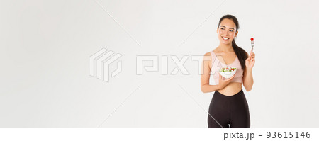 Sport, wellbeing and active lifestyle concept. Happy female athlete, asian fitness girl in activewear holding salad and tomato on fork, smiling, workout coach share diet and perfect body secrets 93615146