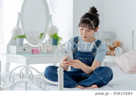 ベッドの上であぐらをかいてスマホを操作する女子高生 ベッドの上であぐらをかいてスマホを操作する女子高生 93615684