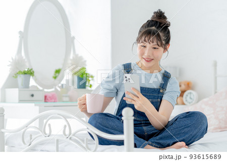 ベッドの上であぐらをかいてスマホを操作する女子高生 93615689